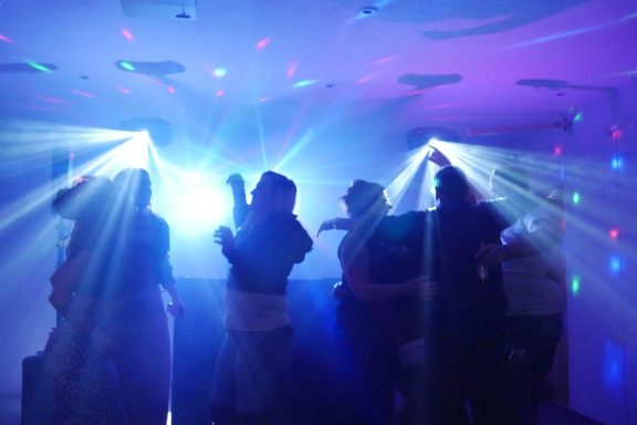 Silhouettes of people dancing under colourful lights at a lively party.