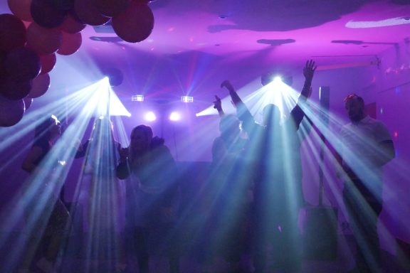Silhouettes of people dancing under colourful lights and beams during a party.