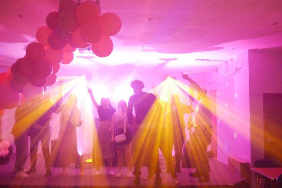 Silhouettes of people dancing under bright pink and yellow stage lights at a party.